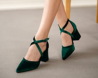 May include: A pair of dark green velvet heeled shoes with criss-cross straps and a buckle closure.