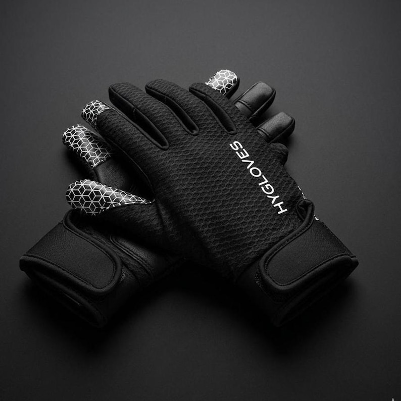 Puede incluir: Guantes negros con superficie texturizada y patrones geom&eacute;tricos blancos en las puntas de los dedos. Los guantes tienen una correa para la mu&ntilde;eca y la palabra "HYGLOVES" est&aacute; impresa en blanco en el lateral.