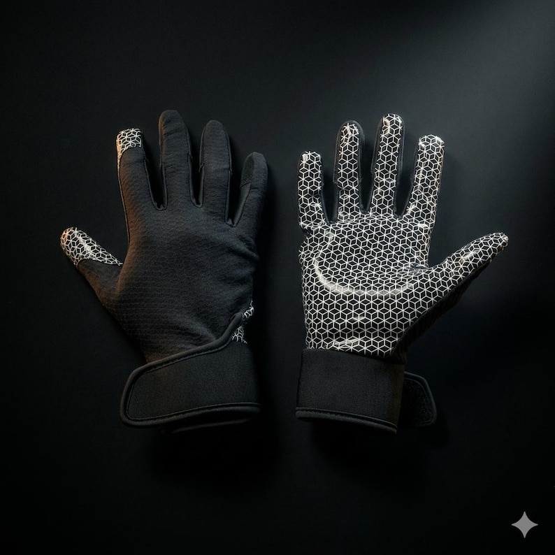 Puede incluir: Un par de guantes negros con una superficie texturizada. Las palmas y las puntas de los dedos presentan un patr&oacute;n geom&eacute;trico blanco. Los guantes tienen una correa de mu&ntilde;eca con cierre de velcro. El fondo es negro.