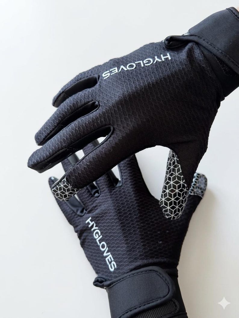 Puede incluir: Guantes negros con el texto blanco "HYGLOVES". Los guantes tienen una superficie texturizada y un patr&oacute;n geom&eacute;trico en las yemas de los dedos y la palma. Tienen una correa de mu&ntilde;eca para un ajuste seguro.