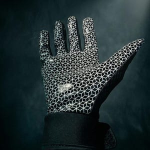 Puede incluir: Guante en blanco y negro con un patr&oacute;n geom&eacute;trico de cubos. El guante tiene un pu&ntilde;o negro y est&aacute; sobre un fondo oscuro. El dise&ntilde;o es un patr&oacute;n repetitivo de cubos blancos sobre una superficie negra.