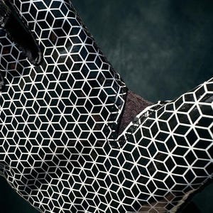 Puede incluir: Primer plano de un guante con estampado en blanco y negro. El guante presenta un dise&ntilde;o geom&eacute;trico de cubos repetidos. El material tiene un acabado brillante y el guante est&aacute; sobre un fondo oscuro.