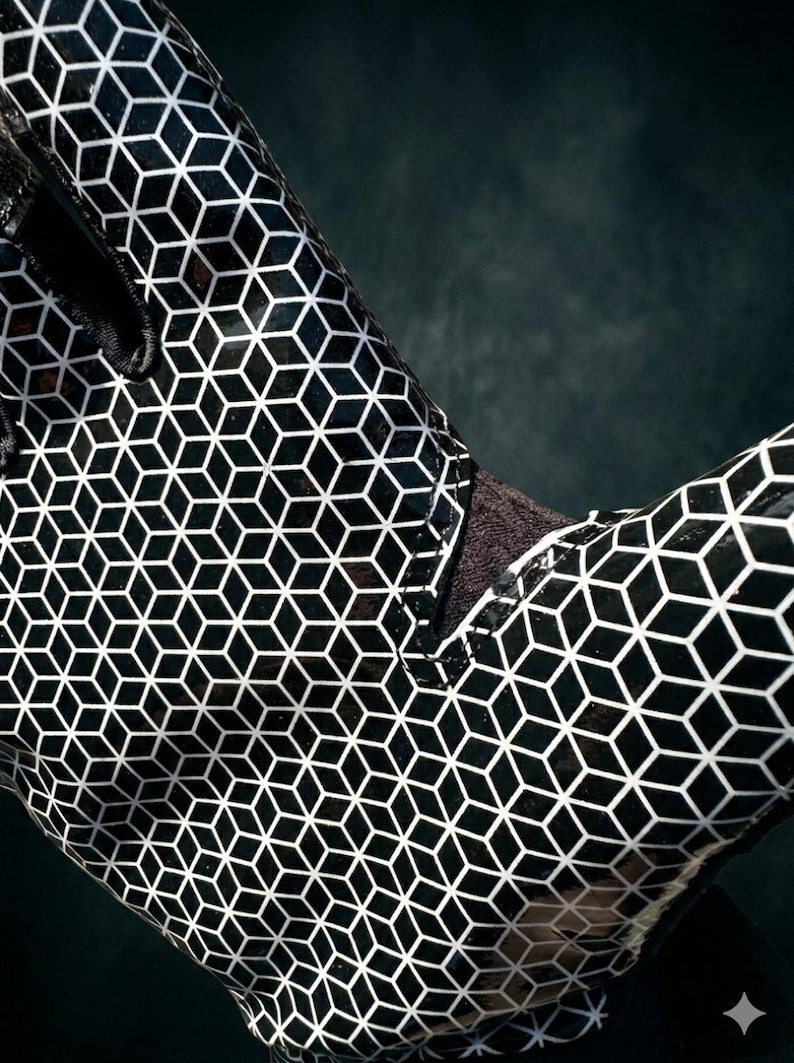 Puede incluir: Primer plano de un guante con estampado en blanco y negro. El guante presenta un dise&ntilde;o geom&eacute;trico de cubos repetidos. El material tiene un acabado brillante y el guante est&aacute; sobre un fondo oscuro.
