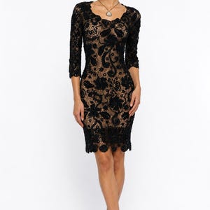May include: A black lace dress with a scalloped neckline and three-quarter sleeves. The dress is knee-length and features a floral pattern. The model is wearing black heels and a necklace.
