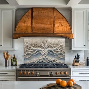 May include: A kitchen with white cabinets, a stainless steel stove, and a copper range hood. A decorative panel with a white tree design is above the stove. Oranges sit on a wooden cutting board on the countertop.