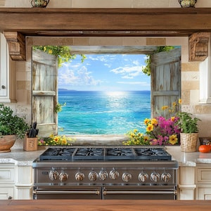 Op de afbeelding: Een keuken met een roestvrijstalen gasfornuis. Het middelpunt is een uitzicht op de zee door een open raam met verweerde luiken, omlijst door bloemen en groen. De keuken heeft witte kasten en een houten balk.