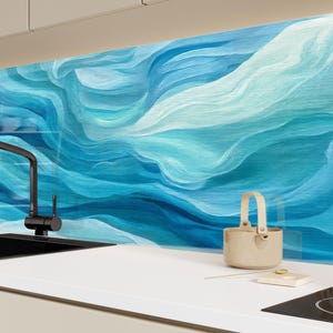 May include: A modern kitchen with a black faucet, sink, and stovetop. The backsplash features a blue and white abstract wave design. A small beige basket and a white cutting board with a gold coin are on the countertop.