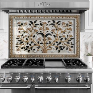 Puede incluir: Un protector contra salpicaduras de cocina decorativo con un diseño de árbol. La obra de arte presenta una combinación de colores dorados, negros y blancos. El protector contra salpicaduras está enmarcado y montado sobre una estufa de gas de acero inoxidable.