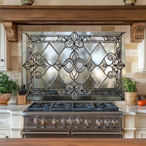 May include: A decorative kitchen backsplash with a stained glass design featuring a fleur-de-lis pattern. The glass is set within a black metal frame. The kitchen also includes a stainless steel range and cream-colored cabinets.