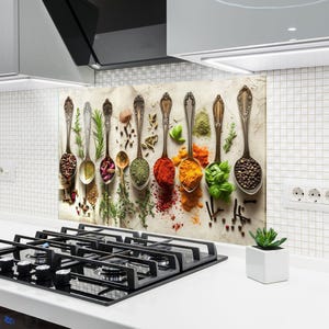 Op de afbeelding: Een keukenachterwand met een verzameling antieke lepels gevuld met diverse kruiden en specerijen. De lepels zijn in een rij gerangschikt en tonen een kleurrijk scala aan ingrediënten zoals paprika, kurkuma en basilicum. De achtergrond is een neutraal, getextureerd oppervlak.