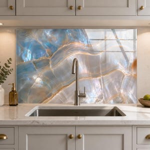 May include: A kitchen backsplash panel featuring a polished, iridescent blue and white marble pattern with gold veining, positioned behind a stainless steel gooseneck faucet and a rectangular undermount sink set into a light-colored countertop.