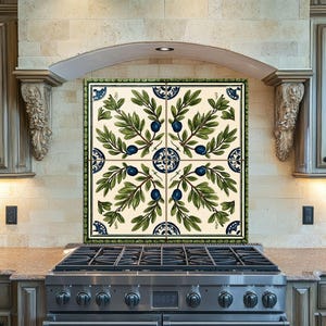 May include: Decorative kitchen backsplash tile with a repeating pattern of olive branches, green leaves and blue olives. The tile has a green border and is above a stainless steel gas range.