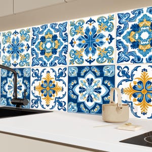 Puede incluir: Azulejos decorativos con un patrón floral azul, blanco y dorado. Los azulejos están dispuestos en una cuadrícula y se instalan como protector contra salpicaduras sobre una encimera blanca. Se ve un grifo y un fregadero negros.