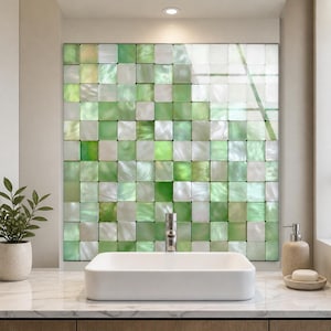 Puede incluir: Una instalación de pared con una cuadrícula de azulejos cuadrados en varios tonos de verde claro, verde oscuro y blanco iridiscente. Los azulejos tienen un acabado brillante y reflectante, dispuestos en un patrón uniforme tras un lavabo.