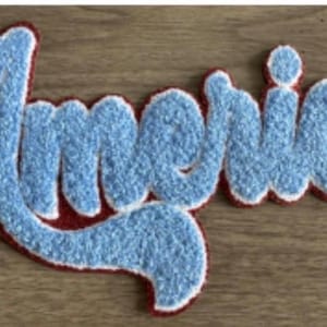May include: A light blue, textured patch with the word "Americas" in a cursive font. The patch has a red border with a white outline, and is set against a wooden background. The patch is likely for clothing or accessories.