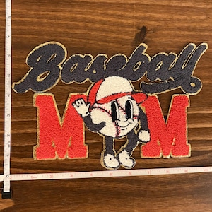 May include: A chenille patch featuring the text Baseball MOM in navy blue and red with gold trim. A cartoon baseball character with a red cap and limbs is positioned in the center. A white measuring tape shows the patch is 8 inches wide and 6 inches tall.