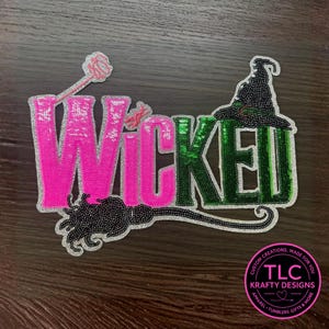 May include: A sequined patch with the word "WICKED" in pink and green, featuring a witch's hat, a broom, and a wand. The patch is outlined in silver and includes the text "TLC Krafty Designs" in a circular logo.