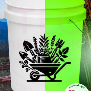 May include: A white plastic bucket featuring a black graphic of a wheelbarrow filled with gardening tools and plants. The bucket glows neon green in the dark. A small circular inset shows a pink LED light and a remote control included with the item.