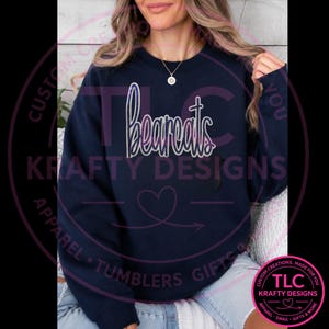 May include: A navy blue crewneck sweatshirt featuring the word Bearcats in a white script font with a subtle purple gradient outline. The garment has long sleeves and a ribbed neckline, providing a classic fit for casual wear and everyday comfort.