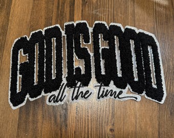 May include: Black and white patch with the text "GOD IS GOOD" in a varsity-style font, with the words "all the time" below. The patch has a textured, fuzzy appearance and a silver border.
