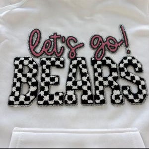 May include: White hoodie with the phrase "let's go BEARS!" in a combination of pink and black and white checkered letters. The letters have a glittery silver outline. The hoodie has a front pocket.