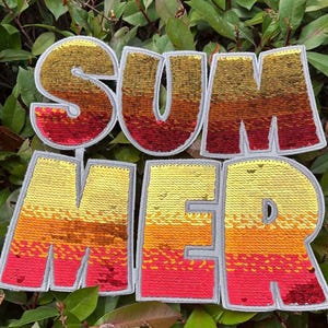May include: A sequined patch spelling "SUMMER" in large, block letters. The letters transition from red at the bottom to yellow at the top, with orange and brown in between. The letters have a gray border and are set against a backdrop of green leaves.