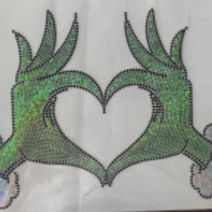 May include: Green hands forming a heart shape, embellished with black rhinestones. The hands have a shimmering, iridescent effect. The wrists are red with a silver, glittery cuff. The design is on a white background.