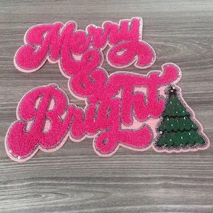 May include: A pink, sequined patch with the words "Merry & Bright" in a cursive font. A green Christmas tree with sequin ornaments is on the right. The patch has a black border and is on a gray wooden surface.