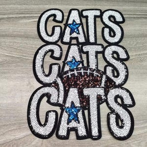 May include: Embroidered patches spelling "CATS" in white sequins with black borders. A sequined football and blue star accents are featured. Ideal for apparel and accessories.