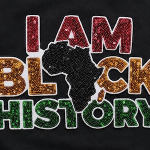 May include: Black background with the words "I AM BLACK HISTORY" in sequined letters. The word "I AM" is in red sequins, "BLACK" in gold, and "HISTORY" in green. A black sequined outline of the African continent is in the center.