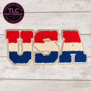 May include: A patriotic USA patch with red, white, and blue sections. The letters are outlined in a glittery gold. The patch is made by TLC Krafty Designs.