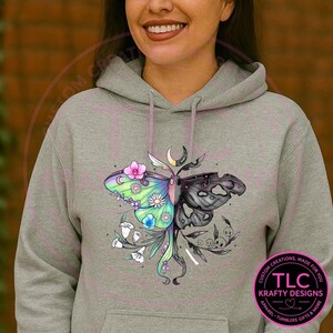 May include: A gray hooded sweatshirt featuring a colorful moth design. The moth is split, with one side vibrant green, blue, and pink, and the other black. The design includes flowers, a crescent moon, and the text "TLC Krafty Designs".