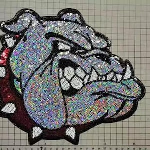 May include: A sequined patch in the shape of a bulldog's head. The patch features iridescent sequins in shades of silver, black, white, and red. The bulldog has a fierce expression, with detailed features and a black outline.