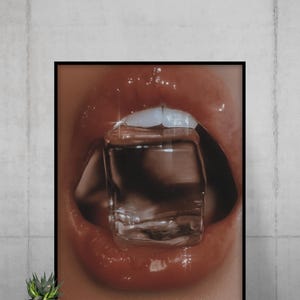 Può includere: Stampa incorniciata con un primo piano di labbra rosse lucide con un cubetto di ghiaccio trasparente tenuto tra i denti. L'immagine ha una messa a fuoco morbida e un'estetica glamour, con riflessi.