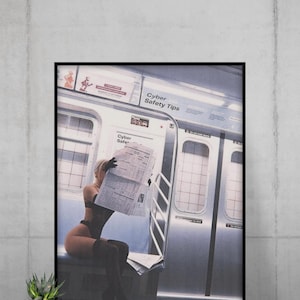 May include: Framed print featuring a woman in lingerie reading a newspaper inside a subway car. The image has a vintage aesthetic with muted tones. The subway car has silver doors and the text "Cyber Safety Tips".