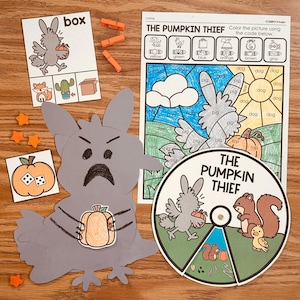 May include: Educational activity set titled The Pumpkin Thief featuring a gray paper cutout character holding a pumpkin, a color-by-code worksheet, a circular spinner with animal illustrations, a small square card with a pumpkin, and three orange clothespins.
