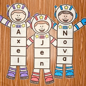 May include: Three astronaut-themed cutouts with names spelled out in block letters. The names are Axel, Jen, and Nova. Each cutout has a star on its helmet and a happy face.