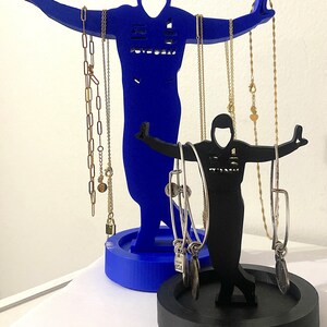 May include: A blue and black jewelry stand shaped like two figures. The larger figure is holding necklaces and the smaller figure is holding bracelets. The stand has a round base.