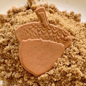 May include: A terracotta acorn-shaped dish sits on a bed of brown sugar crystals.