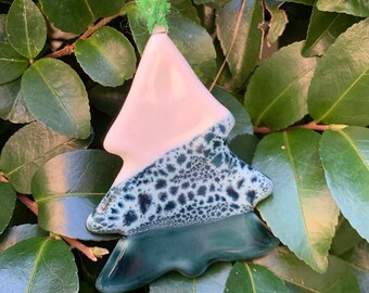 May include: A white and green ceramic Christmas tree ornament with a speckled design. The ornament is hanging from a green ribbon with white snowflakes.