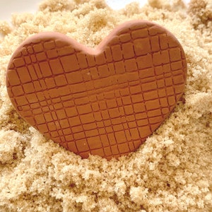 May include: A terracotta heart-shaped ornament with a textured surface, resting on a bed of brown sugar.