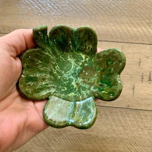 May include: A green ceramic dish shaped like a four-leaf clover. The dish has a marbled green and white glaze.