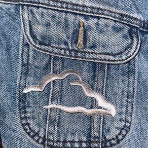 May include: A close-up of a denim jacket with a silver cloud patch sewn onto the pocket.