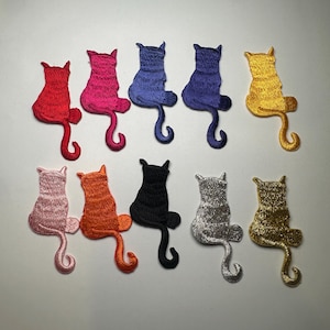 May include: A collection of ten embroidered cat patches in various colors. The patches include red, pink, blue, gold, light pink, orange, black, silver, and gold. Each patch features a cat sitting with its tail curled.