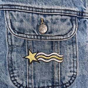 Op de afbeelding: Een gele ster met een witte en gele gestreepte komeetstaart geborduurd op een blauw denim jack.