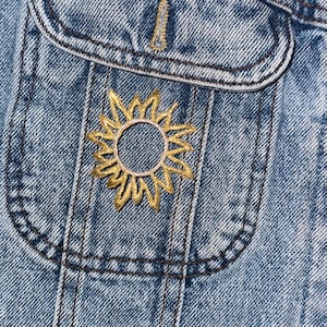 Op de afbeelding: Een spijkerjack met een geborduurde gouden zon op de zak.