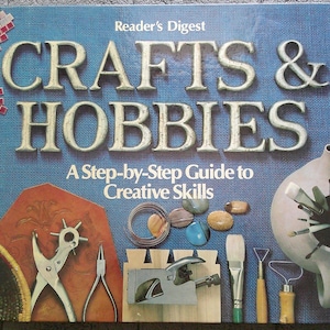 May include: A Reader's Digest Crafts & Hobbies A Step-by-Step Guide to Creative Skills hardcover book with a blue textured cover. The cover features images of various crafting tools including pliers, a paintbrush, a pottery tool, and a ceramic teapot.