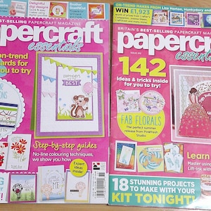 Puede incluir: Dos revistas tituladas "papercraft essentials" con portadas rosas. Una presenta "82 tarjetas de moda" y la otra "142 ideas y trucos". Ambas revistas muestran proyectos de creación de tarjetas, con imágenes de tarjetas y materiales.