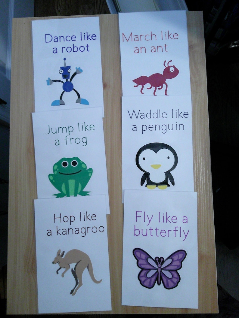 May include: Six white cards with animal illustrations and instructions. The cards read: "Dance like a robot," "March like an ant," "Jump like a frog," "Waddle like a penguin," "Hop like a kangaroo," and "Fly like a butterfly."