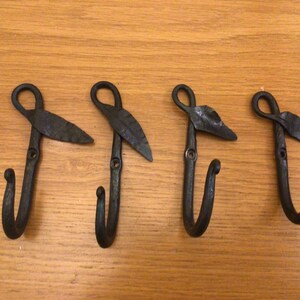 May include: Four black metal hooks with leaf-shaped details. The hooks are mounted on a wooden surface.